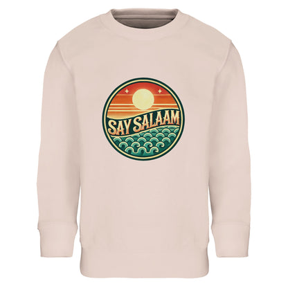 Say Salaam Sunset Glow Part-Recycled Cotton-Poly Kids Sweatshirt in creamy pink, a soft blush tone similar to oyster pink with warm pastel undertones. The bold circular Sunset Glow design contrasts beautifully against the light base, featuring sunset orange sun tones and teal wave details. Crafted from 80% cotton and 20% recycled polyester with brushed fleece lining for added warmth. Ribbed cuffs and hem support long-lasting structure. A confident modest kids sweatshirt for school, sport & everyday styling.