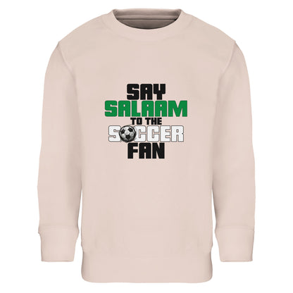 Say Salaam to the Soccer Fan Original Part-Recycled Cotton-Poly Kids Sweatshirt – Creamy Pink / Oyster Pink. Youth Islamic soccer sweatshirt showcasing a stacked text design with bold black and green lettering and a subtle football graphic detail. The vertical layout keeps the message clear and strong, with “Say Salaam” sitting above “Soccer Fan” in a structured, block-style font. Soft pastel tone meets confident sporty typography, blending Muslim identity with grassroots soccer pride for kids on matchdays.